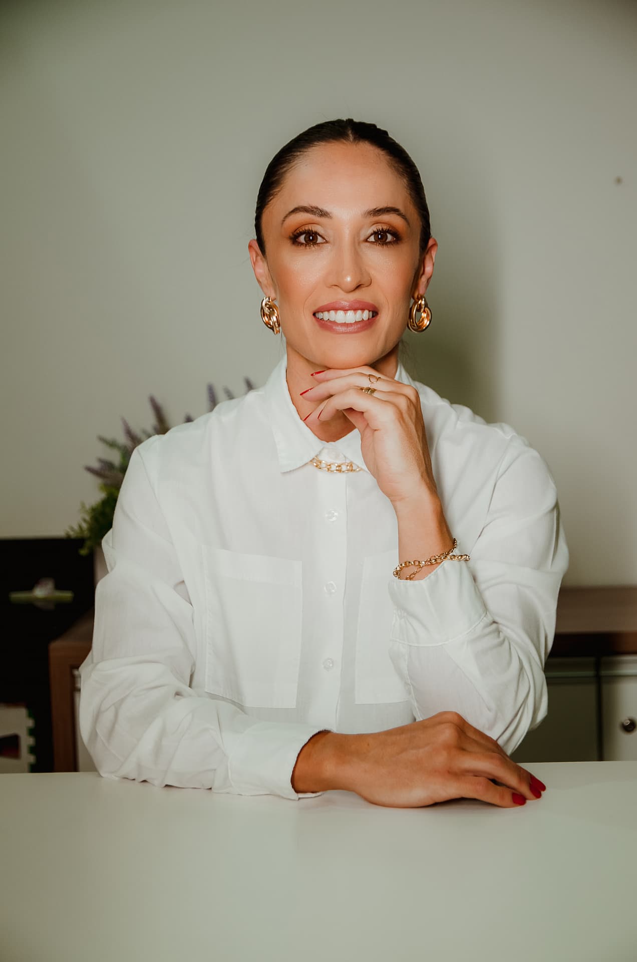 Dra. Marcella Bolognini de camisa branca, sorrindo no consultório