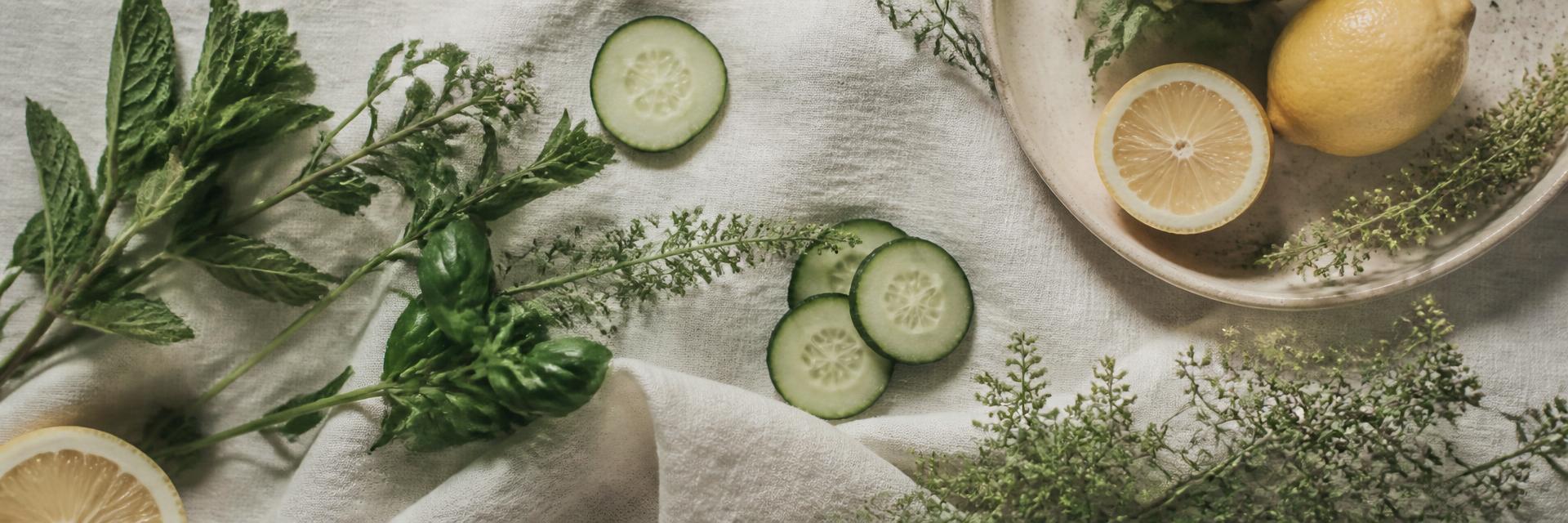 Folhas verdes, ervas frescas, pepino e limão sobre fundo creme